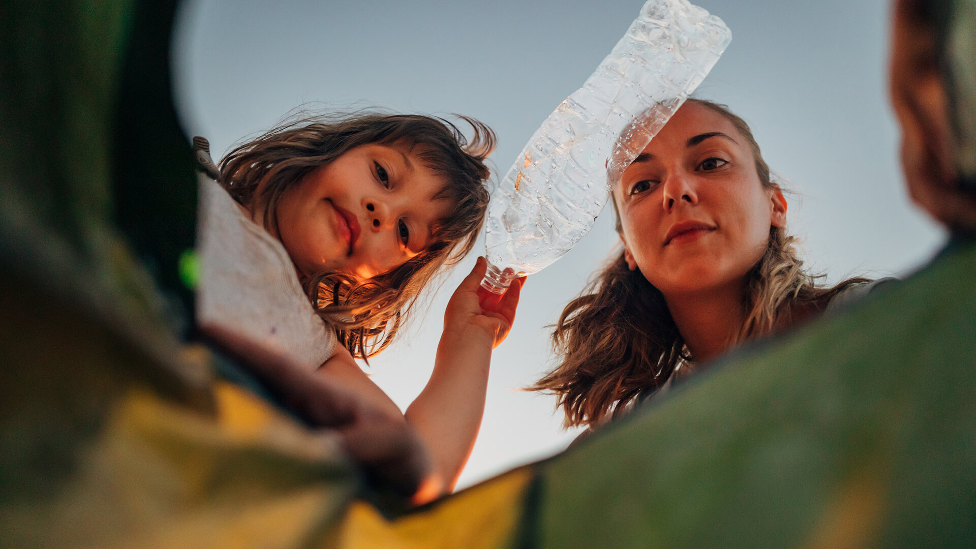 Woman and child placing a plastic bottle into a recycling bin