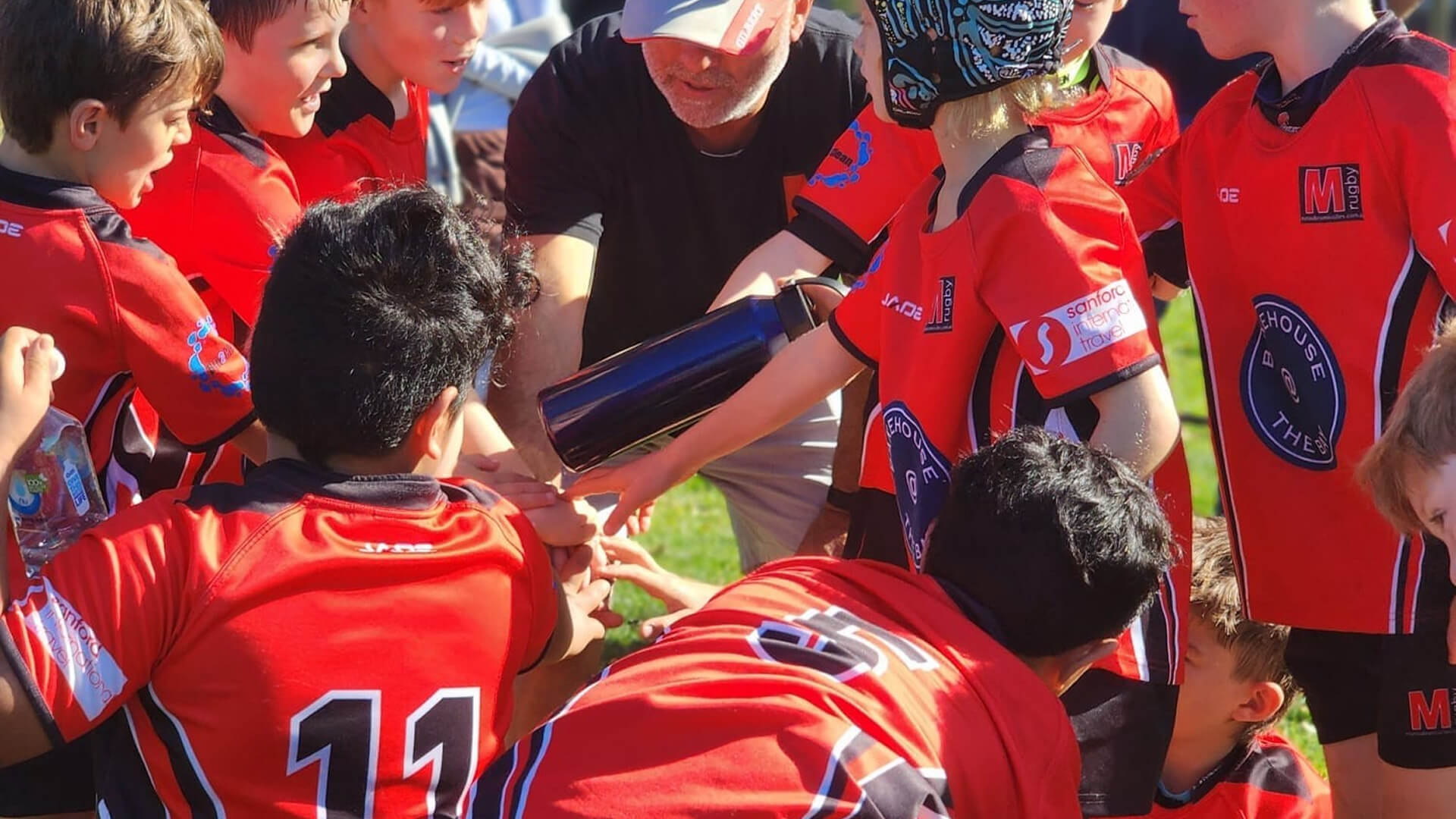 Junior rugby players in red uniforms gathering with their coach